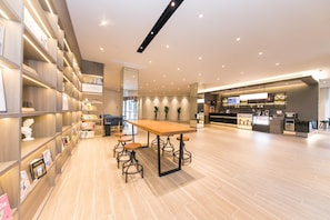 A modern interior with wooden shelves, a central table with stools, and a kitchen area. - Hanting Hotel (Taizhou)