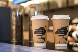 Zwei Papierkaffetassen mit Deckeln und dem Text 'nice café' auf einer spiegelnden Oberfläche.