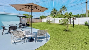 Un patio con mobiliario exterior, una mesa y una sombrilla grande.