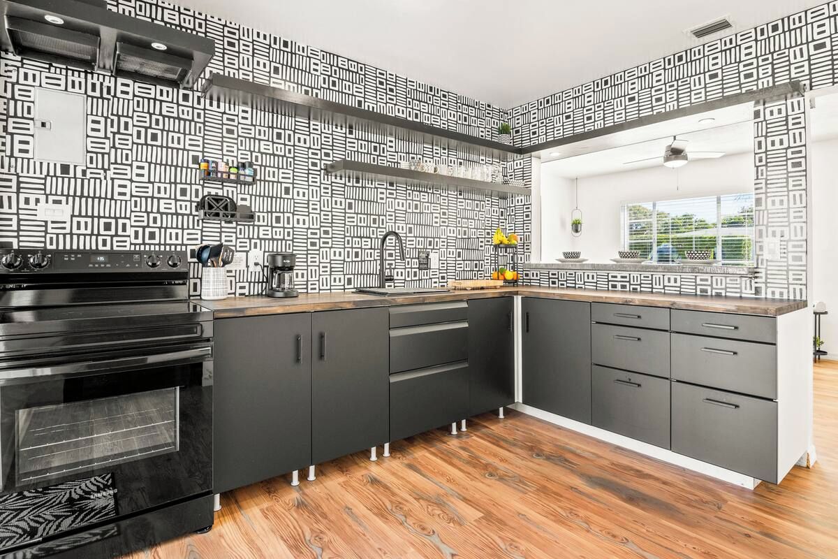 Een moderne keuken met zwarte kastjes, een zwarte oven en een rugpaneel met patroon.