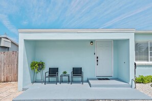A modern house with a light blue exterior, a white door, and a small porch with two chairs and a table.