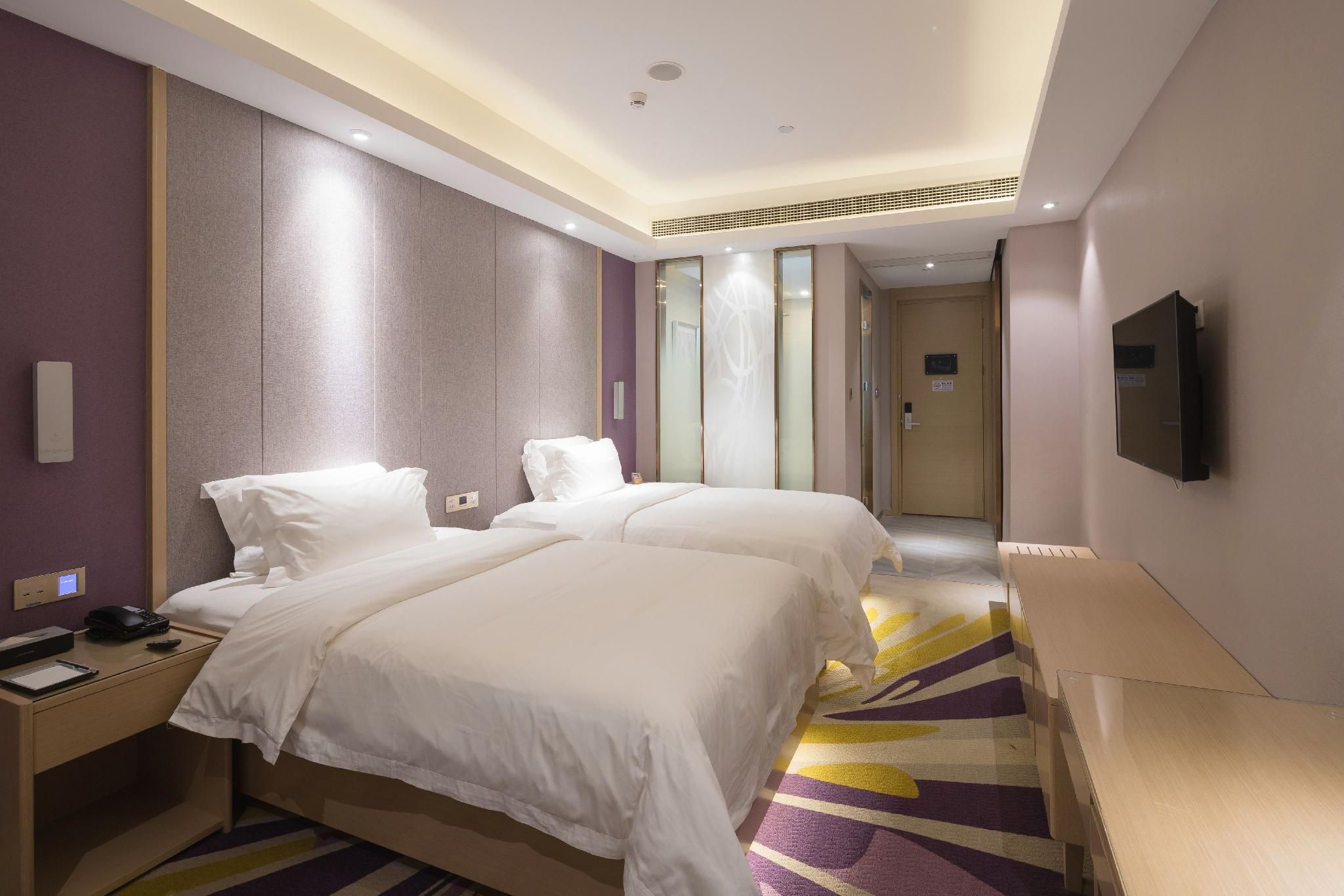 A hotel room with two beds, a desk with a phone and a remote, and a television mounted on the wall.
