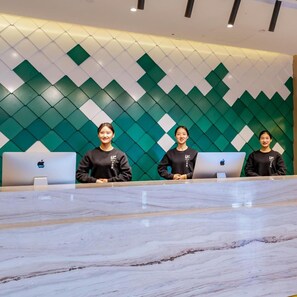 A reception desk with three individuals standing behind it, each with a laptop. The wall behind has a geometric pattern. - Atour Hotel Kunming South High Speed Railway Station University Town (Kunming)
