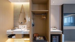 A modern bathroom with a built-in shower, a vanity with a mirror, and a small refrigerator. - Atour Hotel Nankong Quzhou (Quzhou)