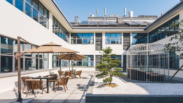 A modern outdoor patio with tables and chairs, a small tree, and a greenhouse structure. - Atour Hotel (Suzhou)