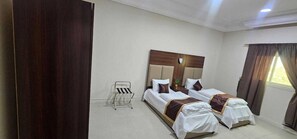 Habitación de hotel con dos camas, cabecera de madera, una mesita y un ventanal con cortinas.