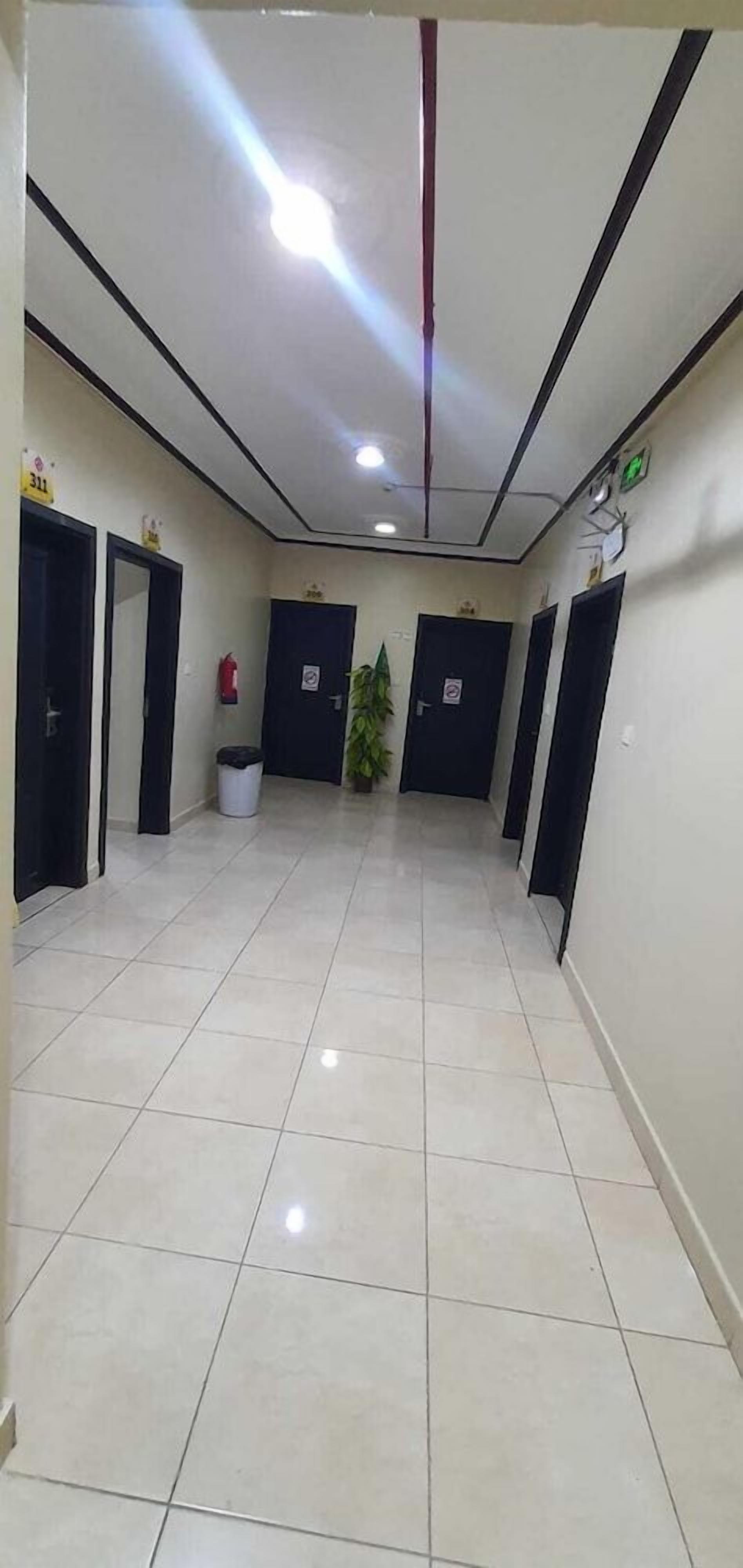 Un pasillo con suelo de baldosas, puertas negras, una planta en maceta y un extintor.