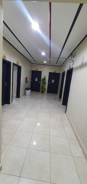 A hallway with tiled flooring, black doors, a potted plant, and a fire extinguisher. - Al Eairy Apartments Al Qassim 1 (Buraydah)