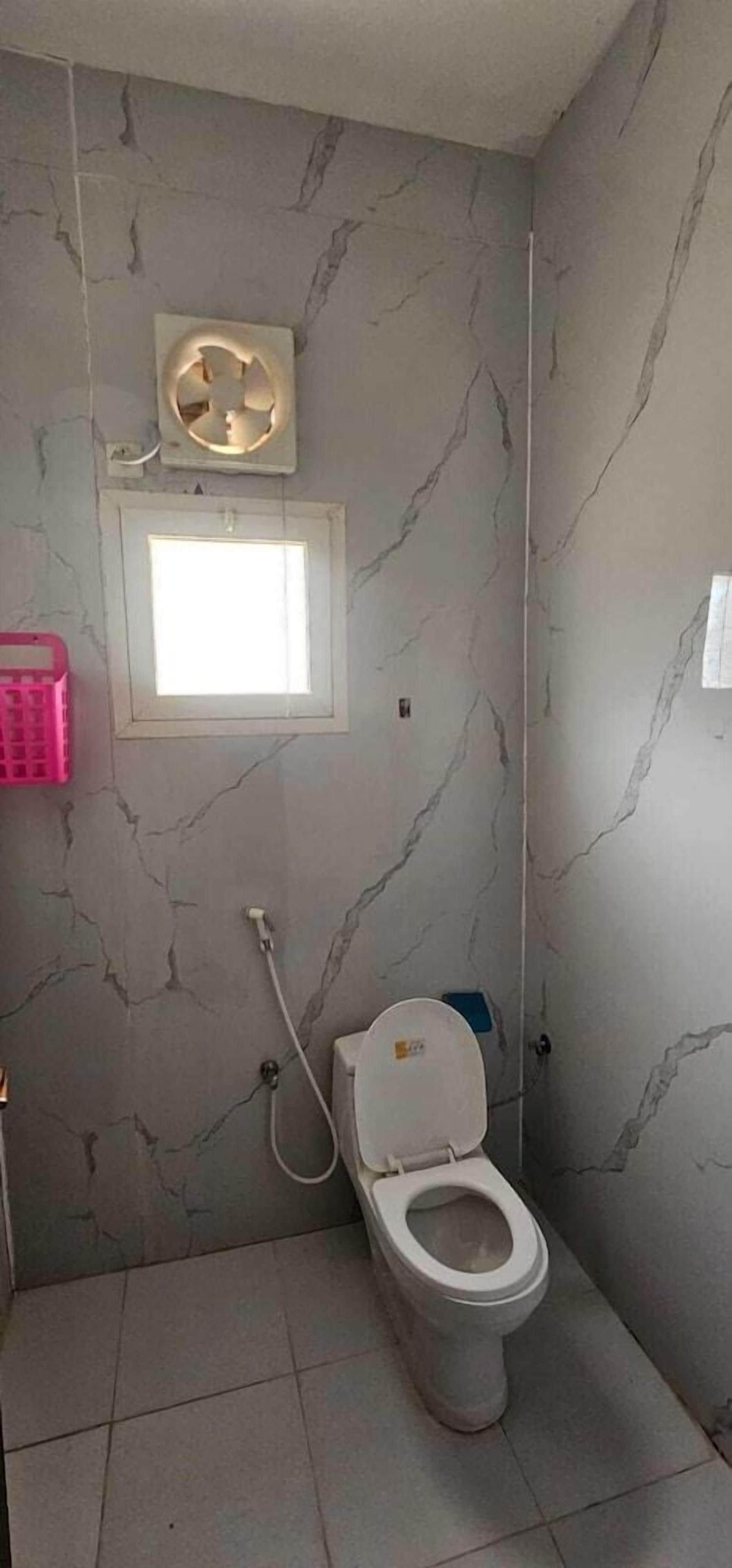 A bathroom with a toilet, a window, and a wall-mounted fan.