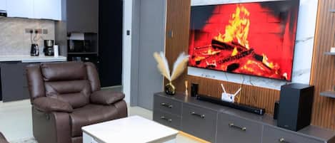 Uma sala de estar moderna com um sofá de couro, uma mesa de centro branca e uma TV de tela plana presa a uma parede de madeira.
