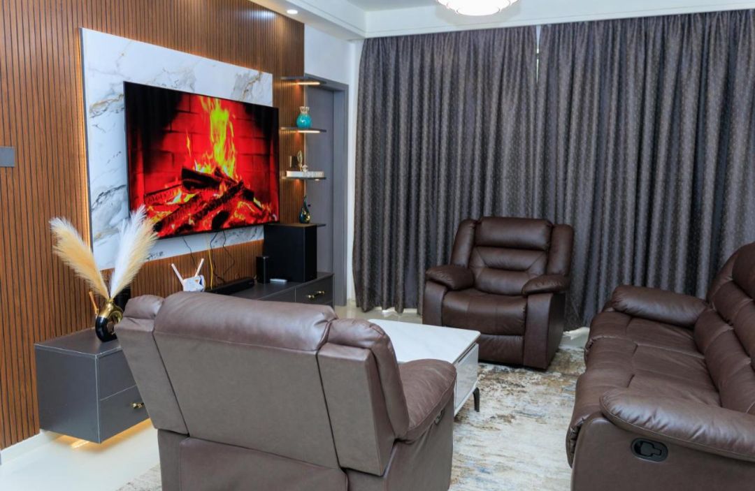 A modern living room with leather sofas, a flat-screen TV, and a fireplace.