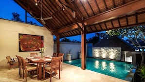 An outdoor dining area with a pool, wooden furniture, and a thatched-roof structure.