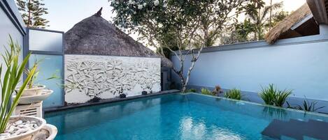 A swimming pool with a stone wall and a thatched-roof structure.