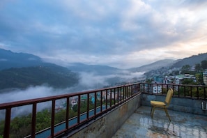A balcony with a metal railing overlooking a mountainous landscape with buildings and a chair. - Mount Himalayan Hotel & Spa Gangtok (Gangtok)