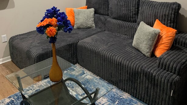 Una sala de estar con un sofá modular, una mesa de centro de vidrio y un jarrón con flores.