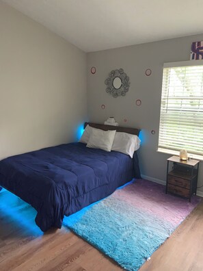 Un dormitorio con cama, mesita de noche, decoración en la pared y ventana.