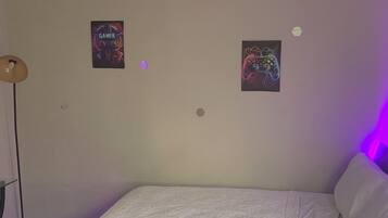 Un dormitorio con cama, dos carteles en la pared y una lámpara de pie.