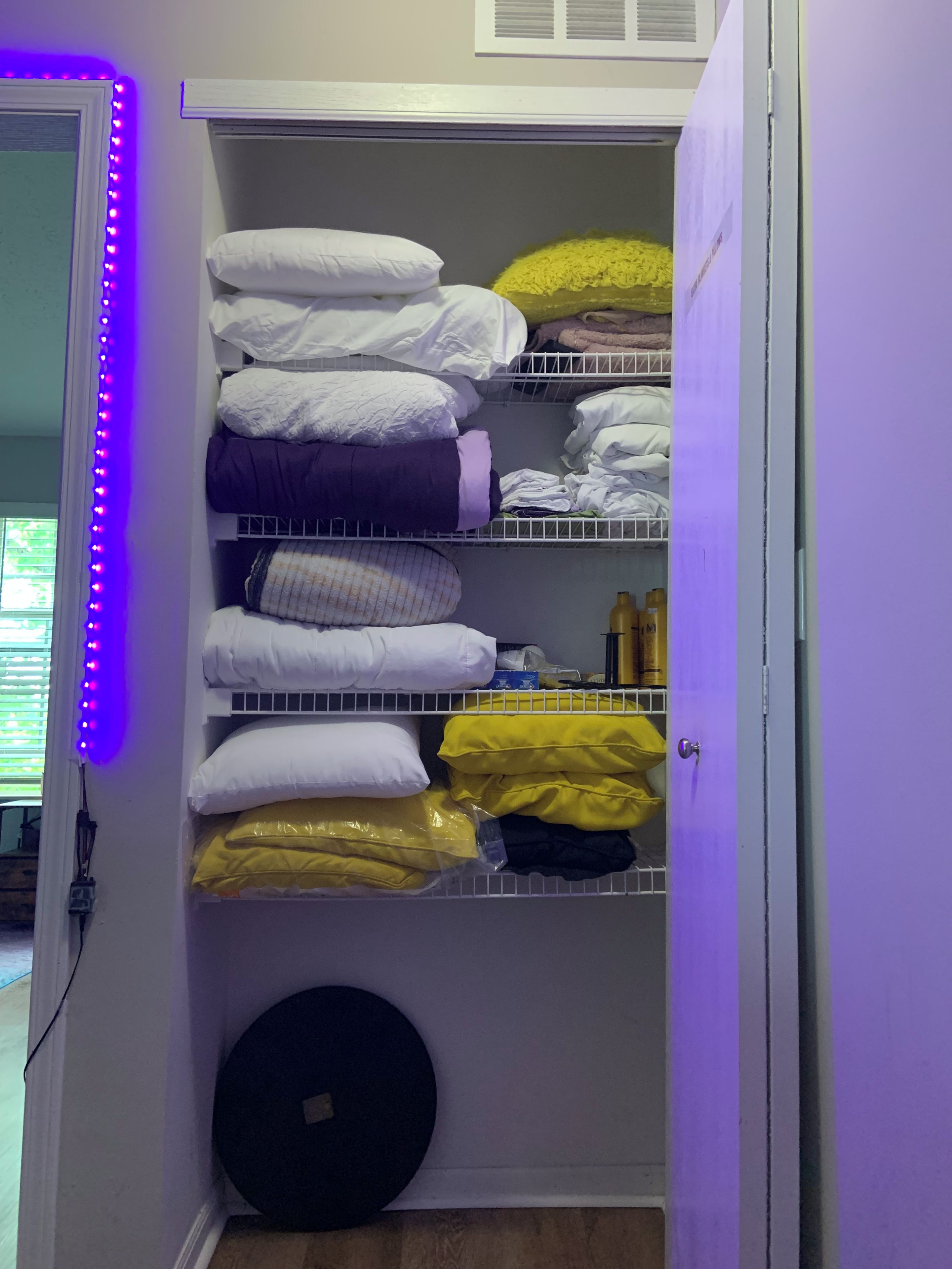 A closet with shelves holding folded clothes and pillows.