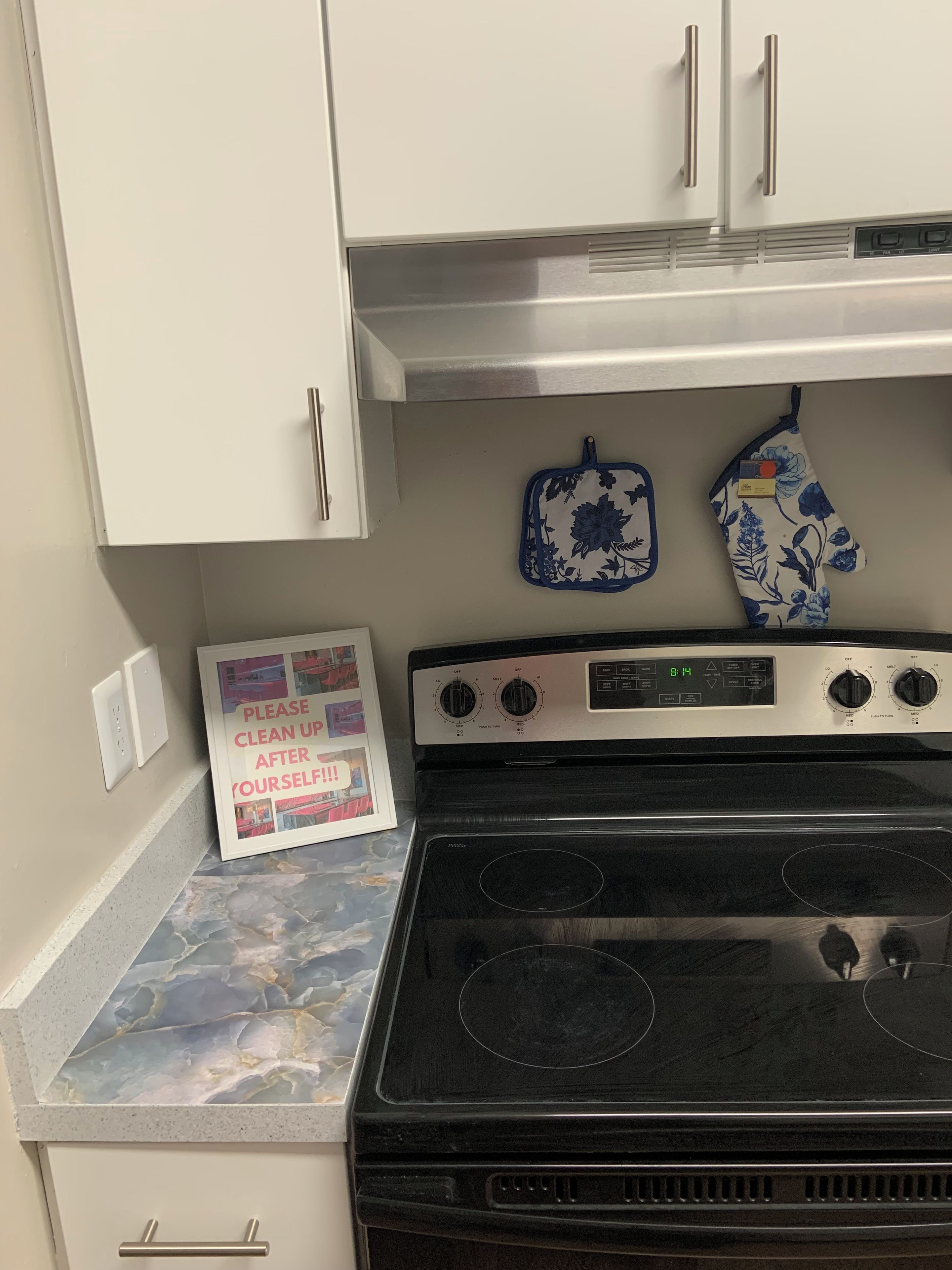 A kitchen with a stove, oven, and two wall-mounted ovens. There is a framed sign on the counter.