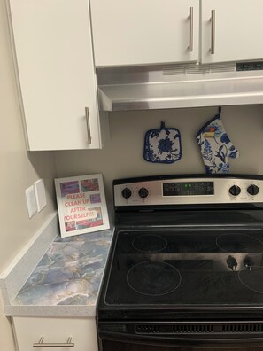 Una cocina con estufa, horno y dos hornos empotrados. Hay un cartel enmarcado sobre la encimera.