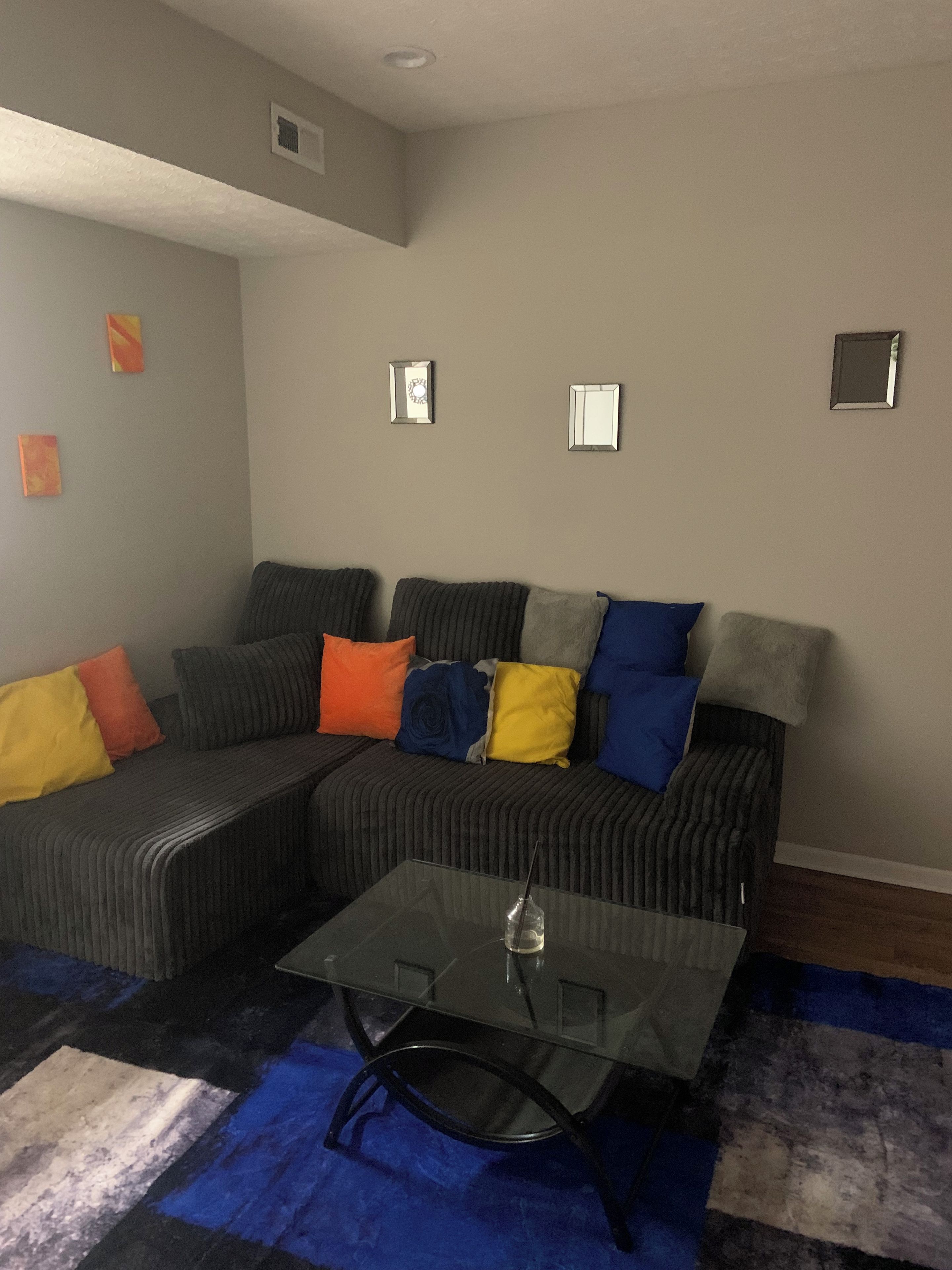 A living room with a sectional sofa, a glass coffee table, and a blue rug.
