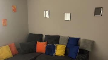 A living room with a sectional sofa, a glass coffee table, and a blue rug.