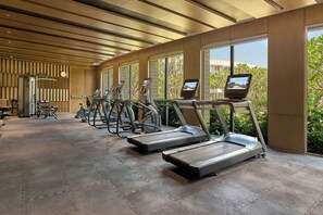A gym with treadmills, exercise bikes, and a wall clock. - Courtyard by Marriott Aravali Resort (Faridabad)