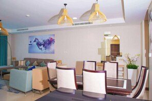A modern living room with a sofa, dining table, chairs, and a large abstract painting. - Gulf Executive Residence Juffair Gerj (Manama)