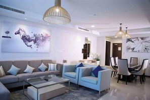 A modern living room with a sofa, coffee table, and a dining area with chairs and a table. - Gulf Executive Residence Juffair Gerj (Manama)