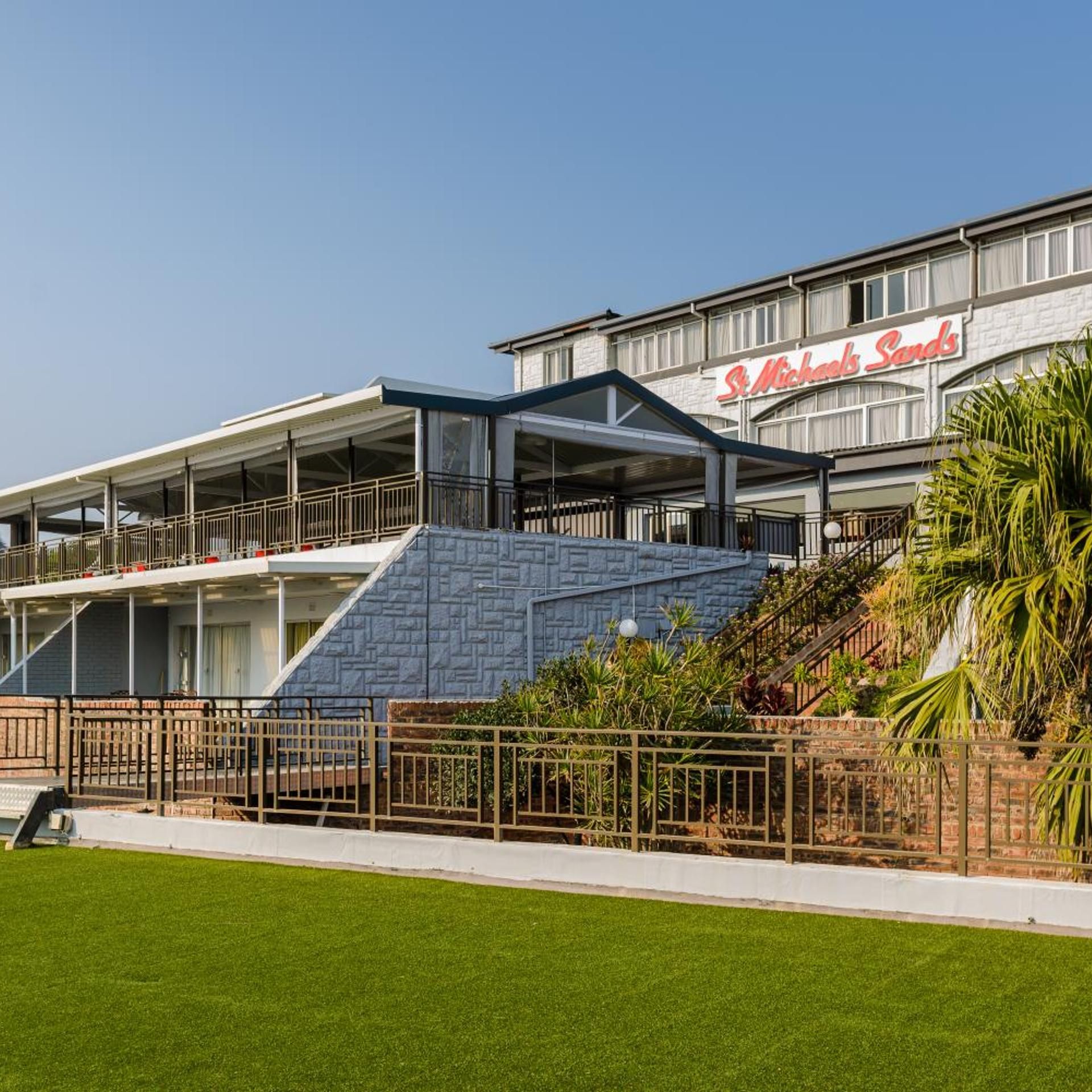 A hotel with a prominent sign reading 'St. Michaels Sands.' It features a modern design with a flat roof and a large, sloped glass facade.