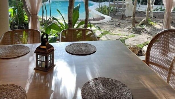 A dining table with woven placemats and a lantern, set against a backdrop of a thatched roof and a view of a pool and greenery. - Pepem Holistic Experience and Chaman Cuisine Restaurant - Adults Only (Tulum)