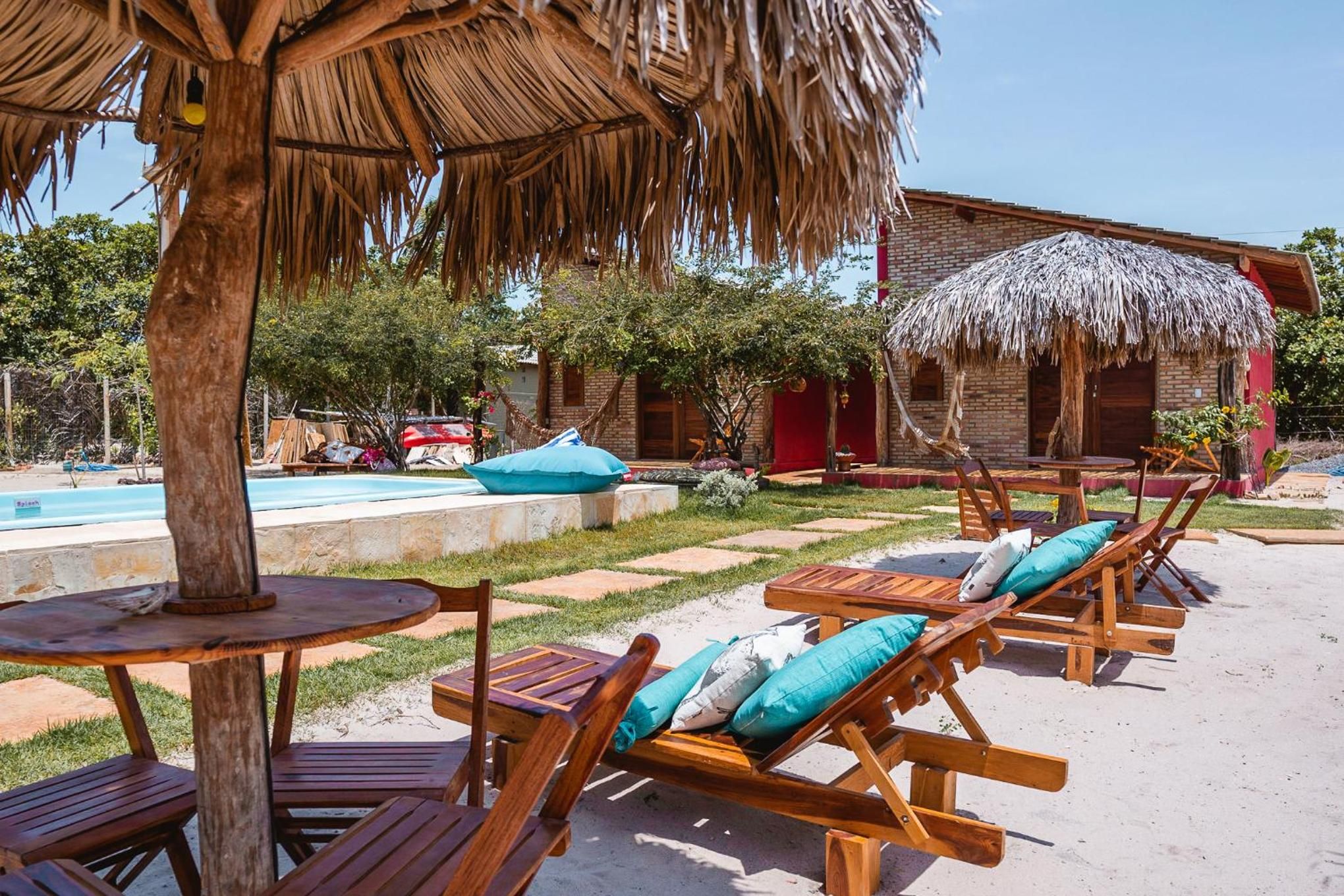 Un resort con sillones de madera y una sombrilla de paja, una piscina y un edificio de ladrillo al fondo.