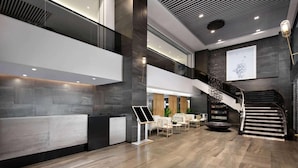 A modern lobby with a reception desk, seating area, and a staircase. - Ramada Encore by Wyndham Jiusuo Downtown (Ledong)