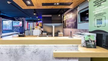 Ein moderner Hotel-Empfangsbereich mit Holzbalkendecke, einer Rezeption, einem Computer und einem wandmontierten Bildschirm.