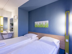 A hotel room with two beds, a bathroom with a sink, and a wall-mounted artwork. - Ibis Budget Saarbruecken Ost (Saarbrücken)