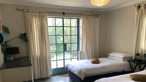 A bedroom with two beds, a window with curtains, a bedside table with a lamp, and a plant. - Tegwaan Country Getaway (Emgwenya)