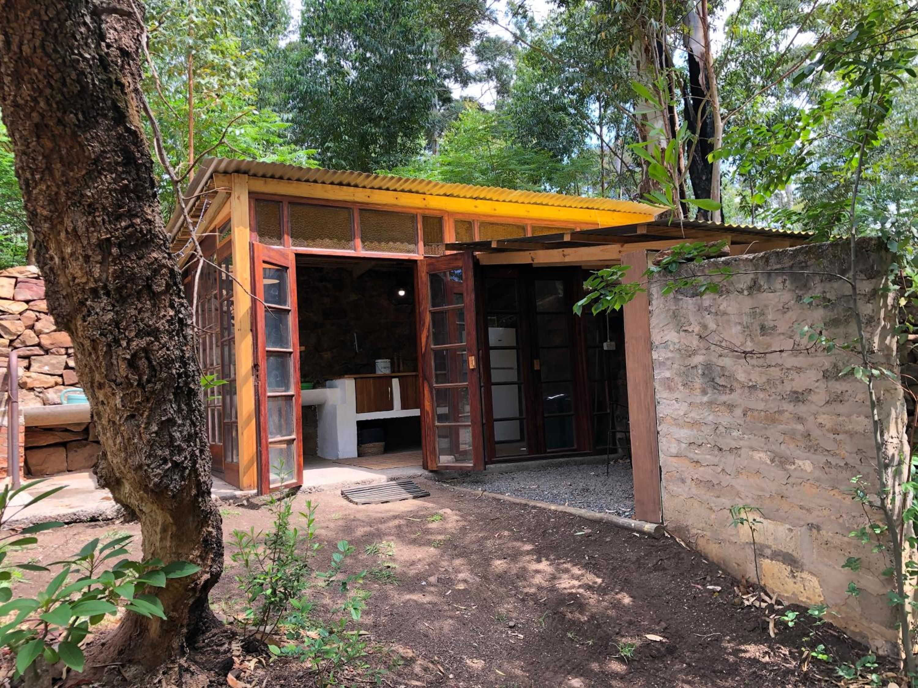 A small wooden structure with a sloped roof, a stone wall, and a tree in the foreground.