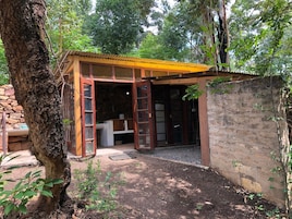 Una pequeña estructura de madera con techo inclinado, pared de piedra y un árbol en primer plano.