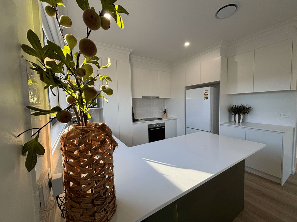 A modern kitchen with white cabinetry, a large island, and a woven basket with fruit.