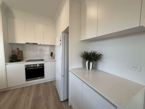 Una cuina moderna amb armaris blancs, forn d'acer inoxidable i un taulell amb una planta en test.