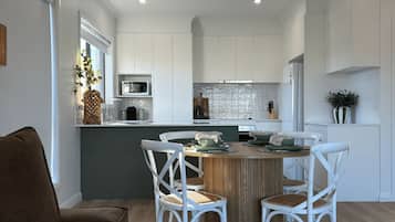 A modern kitchen with white cabinetry, a central island with seating, and a dining area with white chairs.