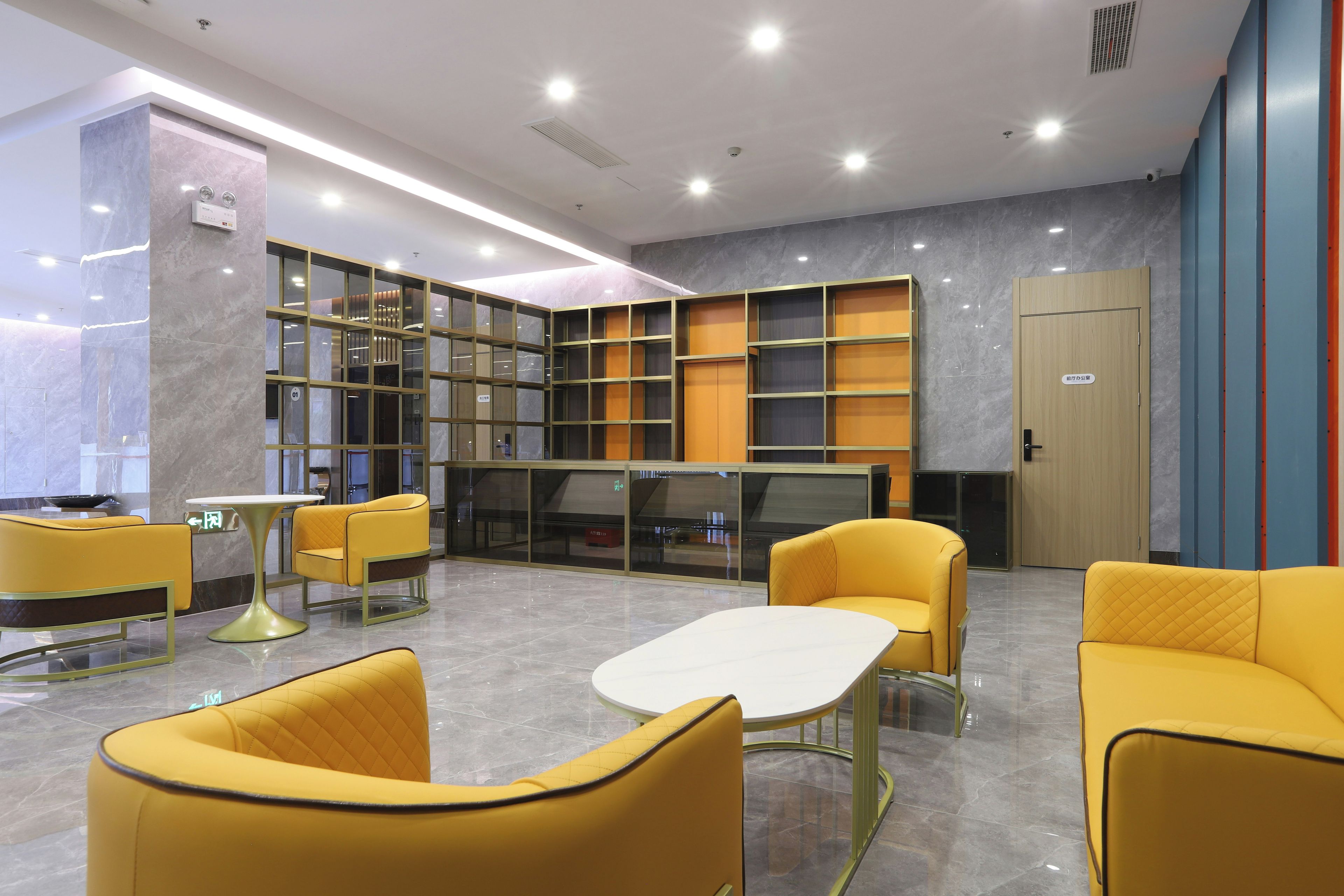 A modern lobby with yellow seating, a reception desk, and a large bookshelf.