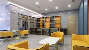 Um lobby moderno com assentos amarelos, uma mesa de recepção e uma grande estante.