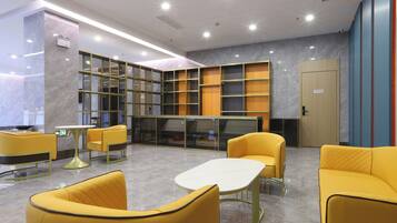 A modern lobby with yellow seating, a reception desk, and a large bookshelf.