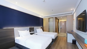 Quarto de hotel com duas camas, televisão, escrivaninha e banheiro visível por uma porta aberta.