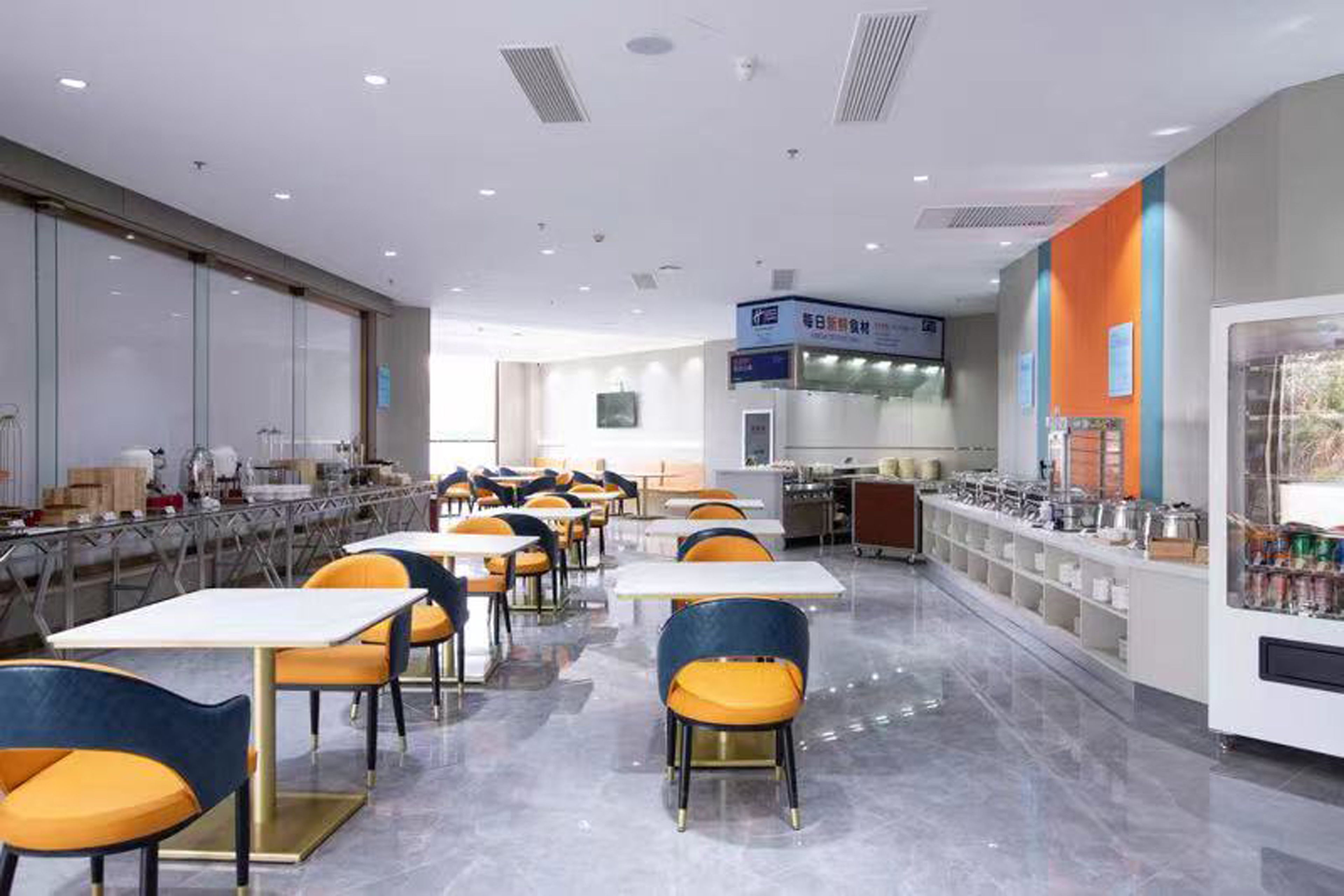 A cafeteria with tables and chairs, a kitchen area, and a vending machine.