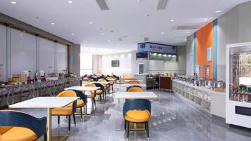 A cafeteria with tables and chairs, a kitchen area, and a vending machine.