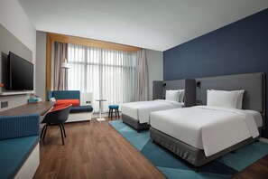 A hotel room with a bed, a desk, a chair, a TV, and a window with curtains.