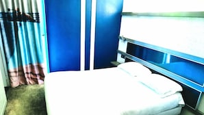 A single bed with a white mattress and pillows, a blue wall, and a window with curtains. - Enzo Hotels Trappes by Kyriad Direct (Trappes)