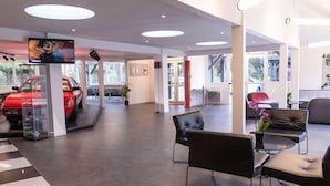 A modern interior with a reception area, seating, and a car display. - Enzo Hotels Trappes by Kyriad Direct (Trappes)